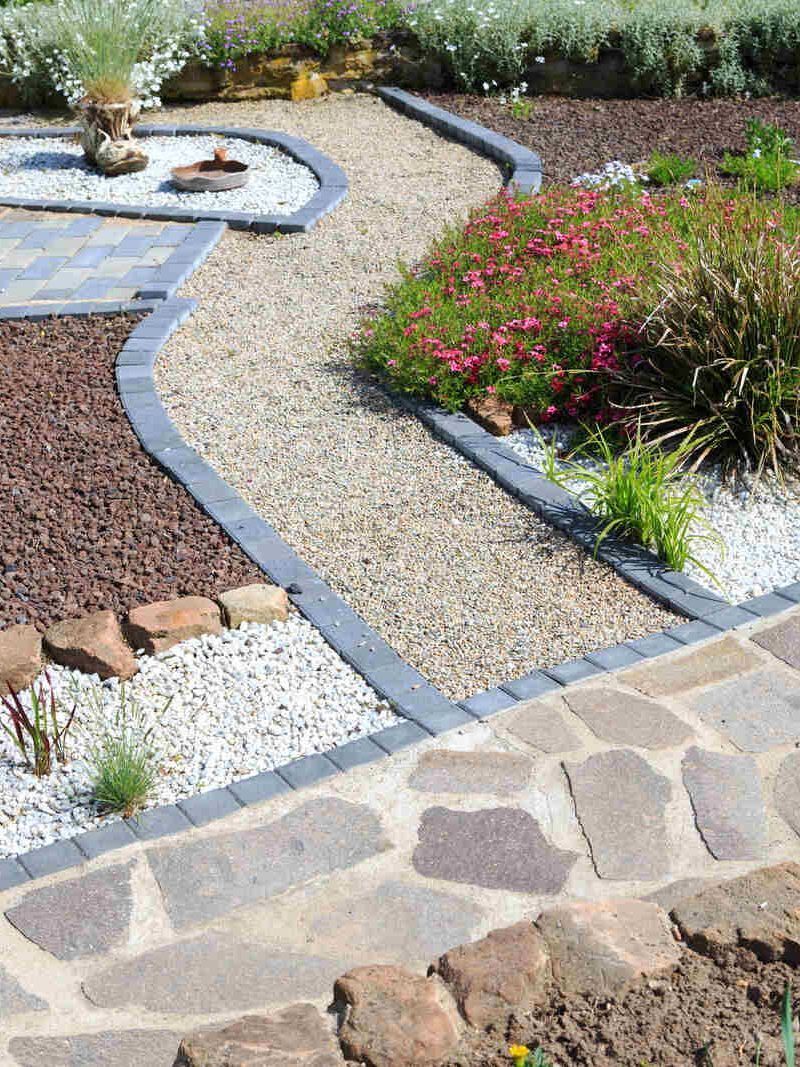 Ein Steinweg in einem Garten, umgeben von Felsen und Blumen.