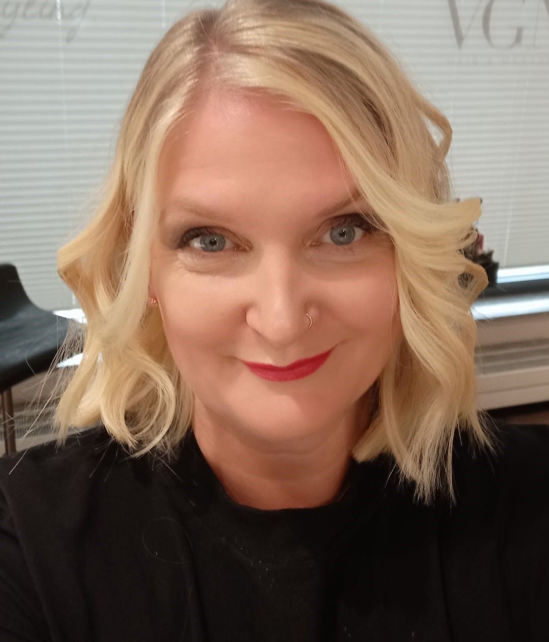 Eine Frau mit blonden Haaren trägt ein schwarzes Hemd und roten Lippenstift.