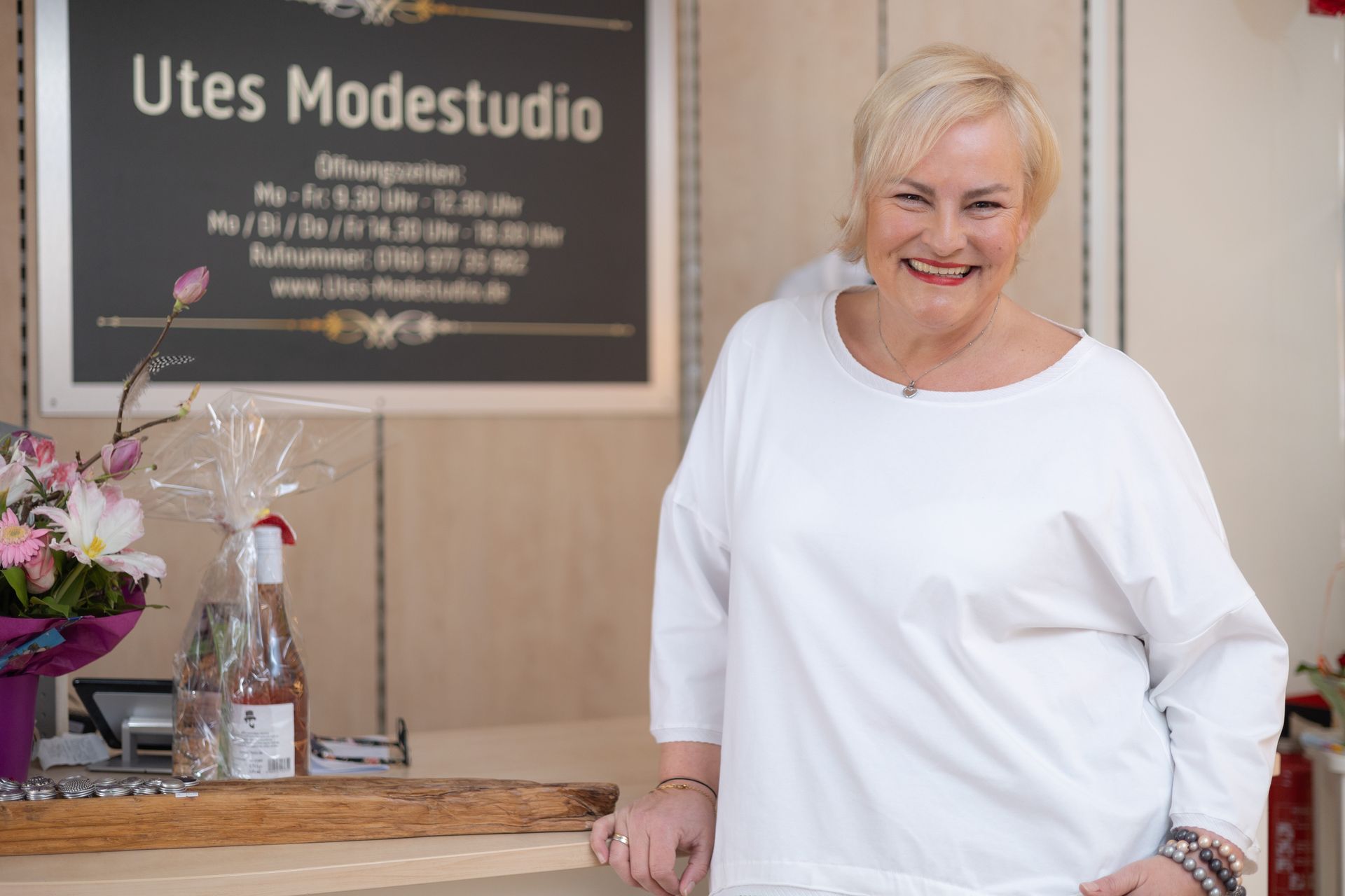 Eine Frau im weißen Hemd steht vor einem Schild.