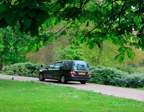 Un coche fúnebre negro circula por una calle en un parque.