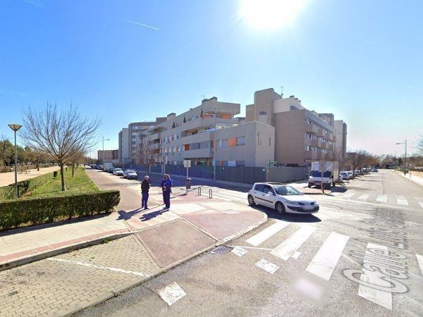 Vista de la calle: peatones en un cruce de peatones frente a edificios de apartamentos en un día soleado.