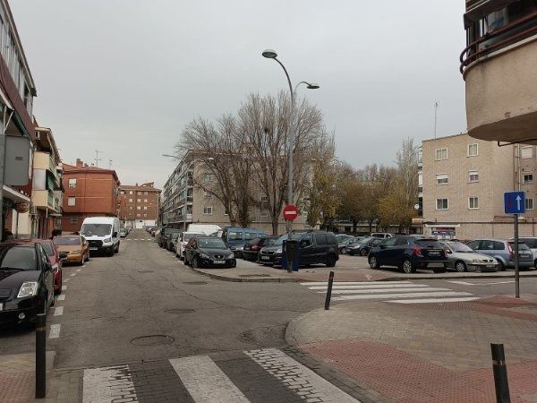 Una escena callejera con autos estacionados, cruce de peatones y edificios de departamentos bajo un cielo nublado.