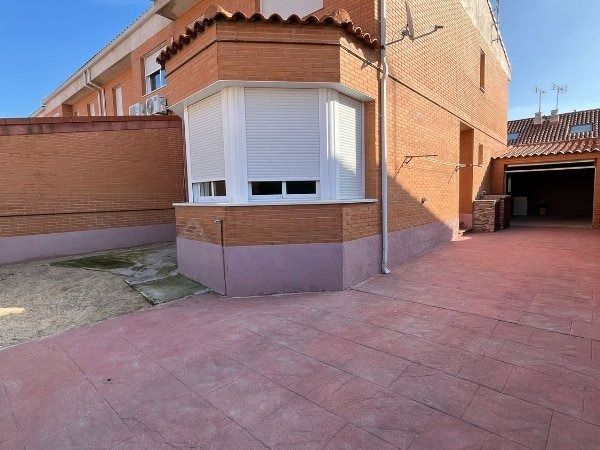 Vista exterior de una casa de ladrillo con ventanal y garaje adjunto. La entrada está roja y el cielo está despejado.