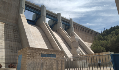 Presa de hormigón con compuertas bajo un cielo nublado, árboles al fondo.