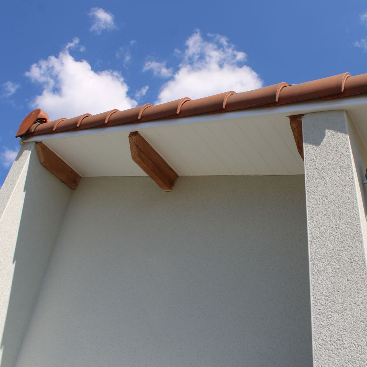 Extérieur du bâtiment avec toit en tuile, poutres et dessous de toit en bois blanc.