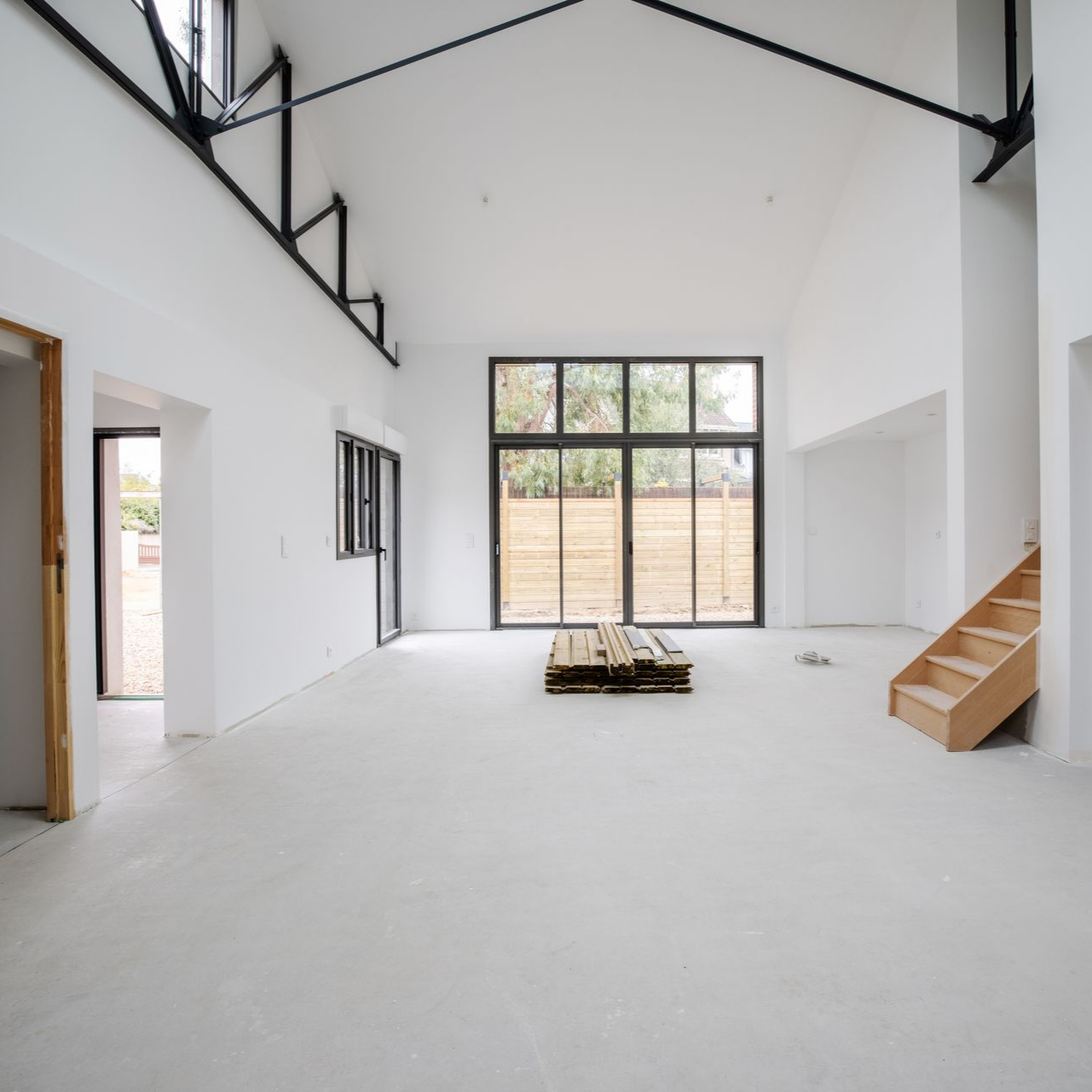 Intérieur ouvert avec de grandes fenêtres, des poutres en acier noir, des escaliers en bois.