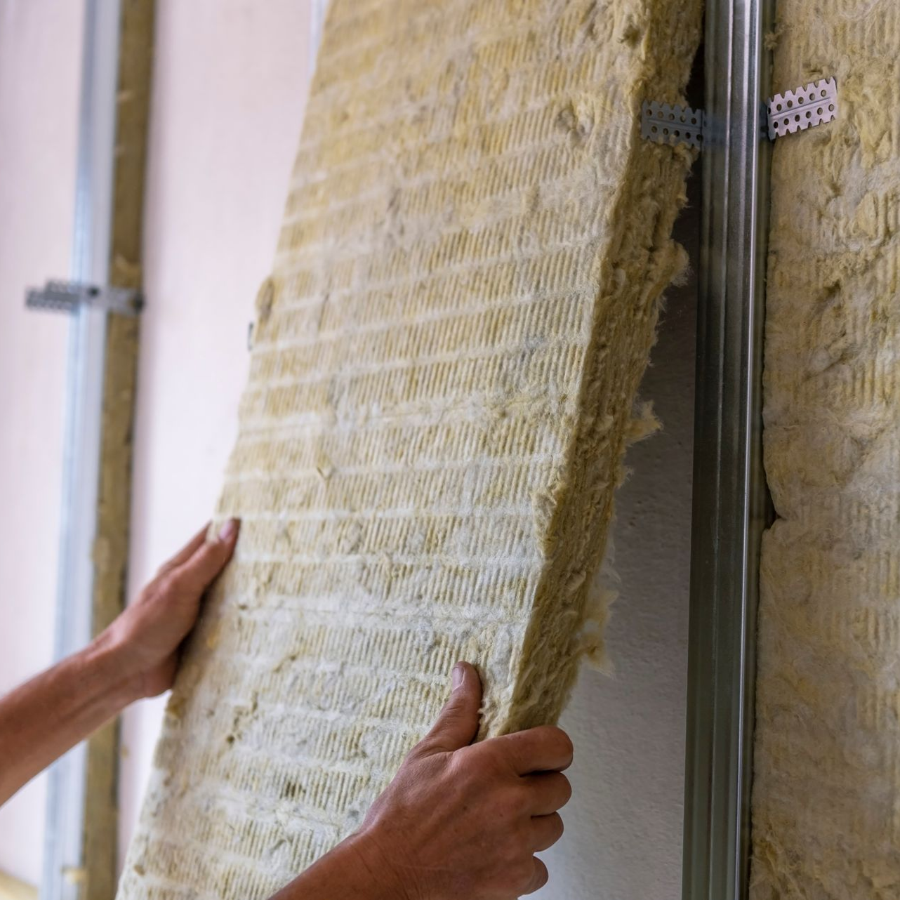Personne installant un panneau isolant dans une ossature murale en métal.