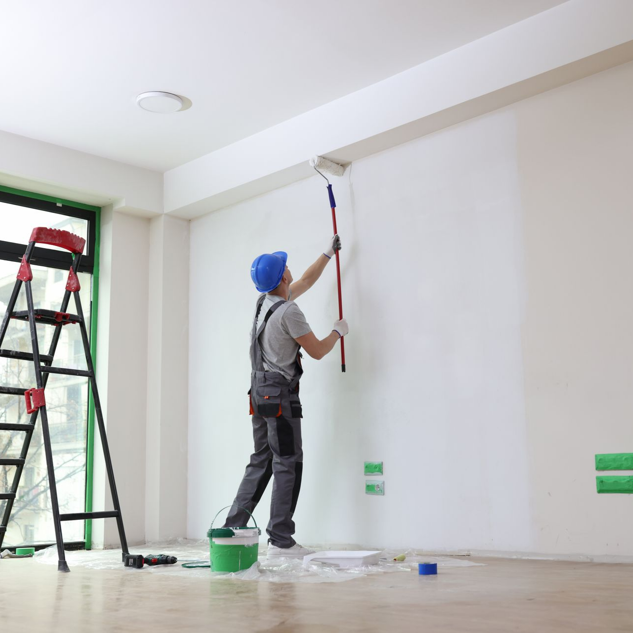 Peintre peignant un mur blanc avec un rouleau, dans une pièce.