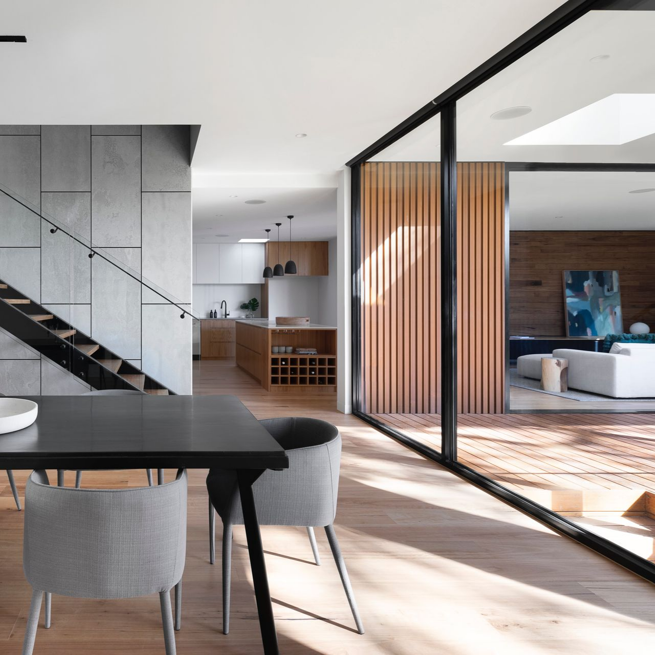 Salle à manger et vue sur un salon avec murs en bois et portes coulissantes en verre.