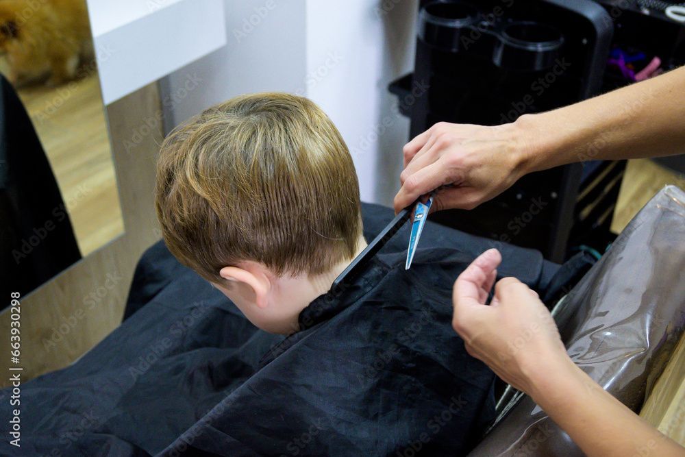 Eine Friseurin schneidet einer Kundin mit einer Schere die kurzen Haare; ein schwarzer Umhang ist über ihre Schultern drapiert.