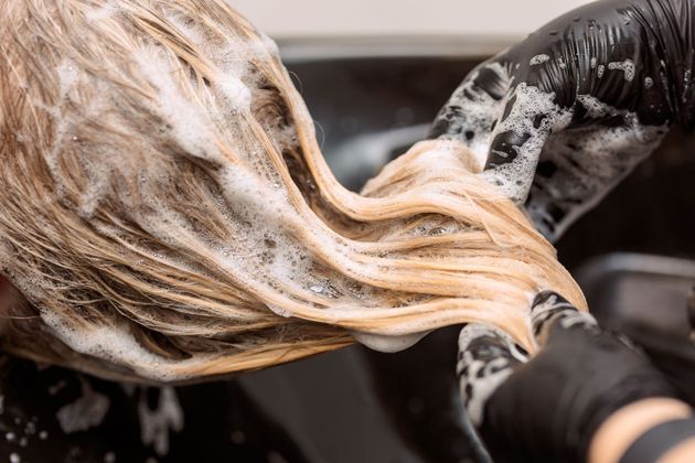 Haare werden im Friseurstuhl mit einem schwarzen Haartrockner geföhnt, langes braunes Haar ist ausgebreitet.