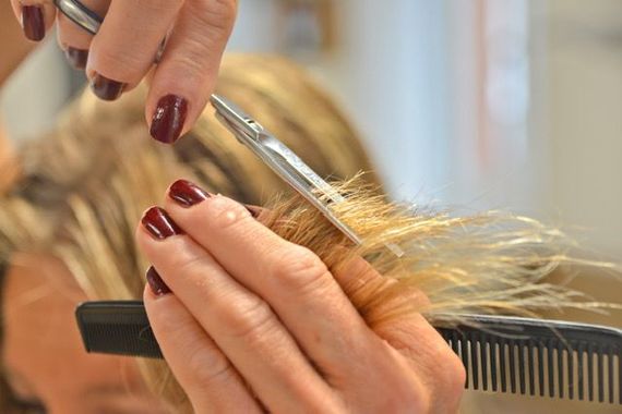 Eine Friseurin schneidet einer Kundin mit einer Schere die kurzen Haare; ein schwarzer Umhang ist über ihre Schultern drapiert.