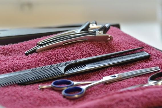 Haare werden im Friseurstuhl mit einem schwarzen Haartrockner geföhnt, langes braunes Haar ist ausgebreitet.