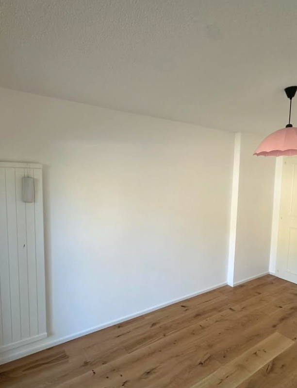 Murs blancs avec parquet et suspension rose dans la chambre.