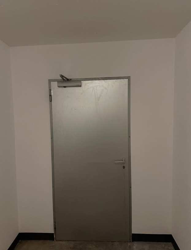 Porte en métal dans un couloir blanc ; la porte a un ferme-porte et une poignée.