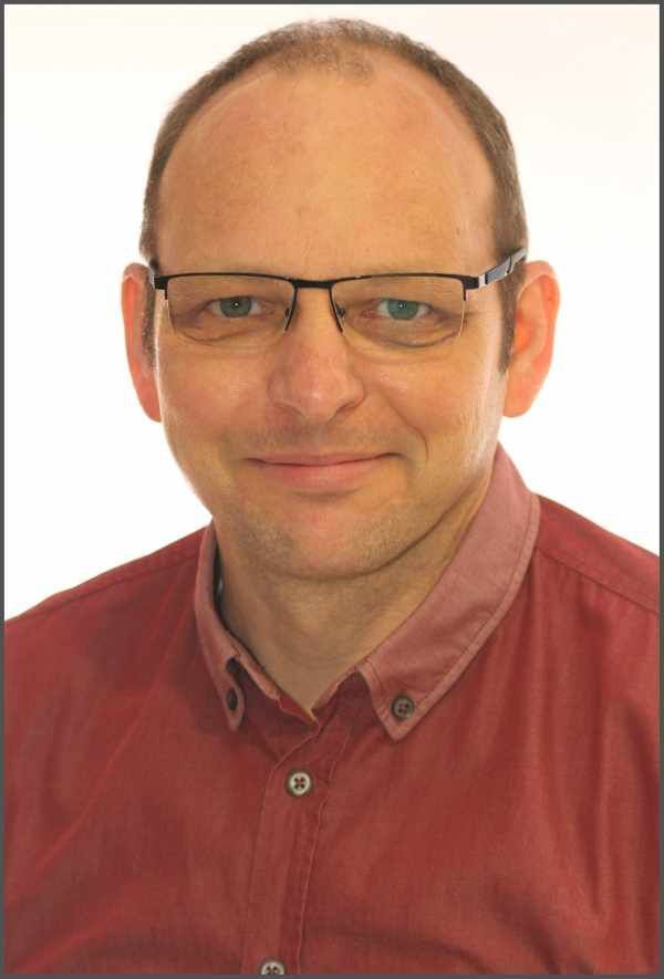 Ein Mann mit Brille und rotem Hemd lächelt in die Kamera