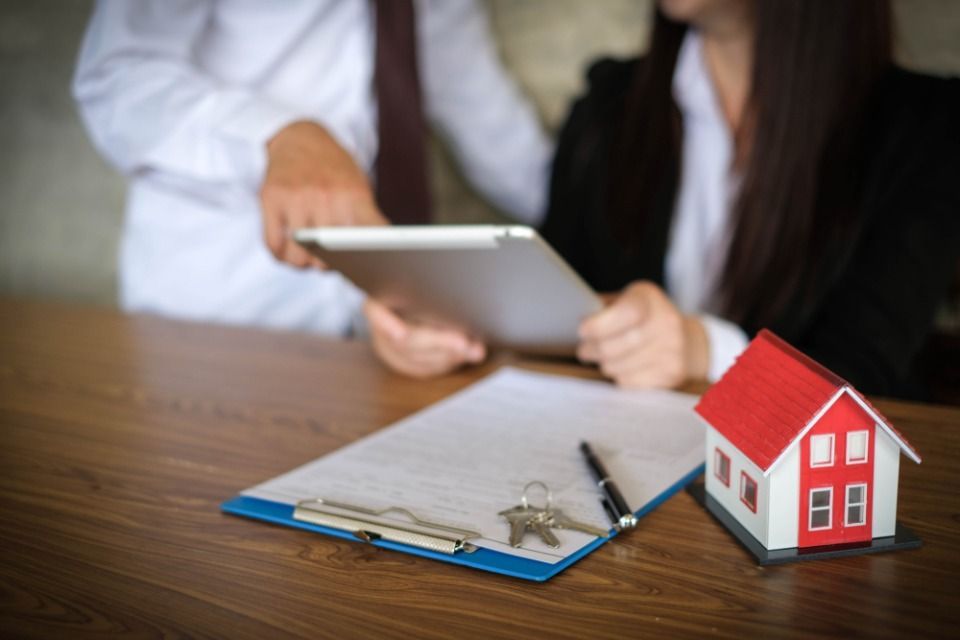 Kleines rotes Modellhaus, Unterlagen und Frau und Mann sehen sich Dokumente an