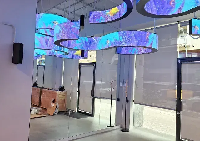Pantallas digitales curvas con escenas submarinas cuelgan del techo en un espacio moderno con puertas de vidrio y una tienda.