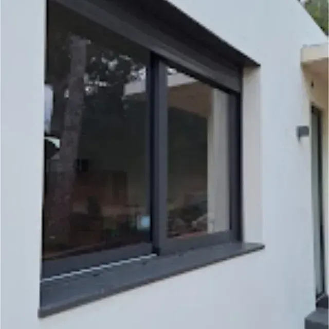 Ventana con marco oscuro en el exterior de un edificio blanco; una persiana oscura cerrada se encuentra sobre el vidrio.