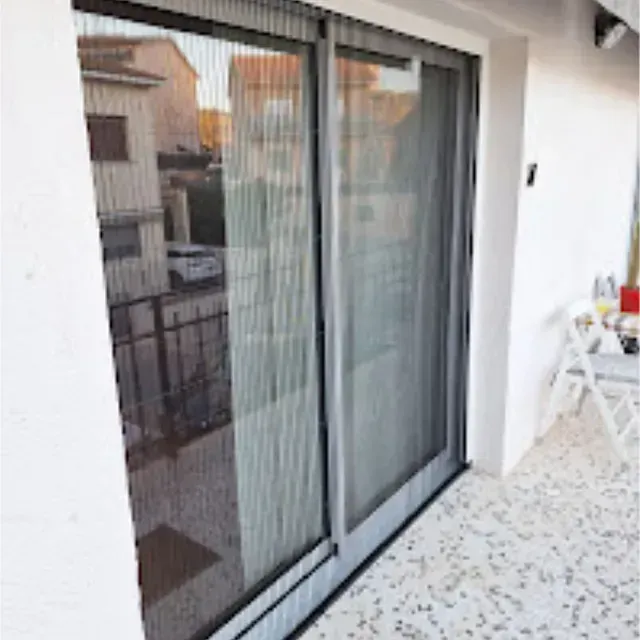 Puertas corredizas de vidrio con mosquitera retráctil sobre una pared de estuco blanco. Exterior con balcón y vista a un edificio.