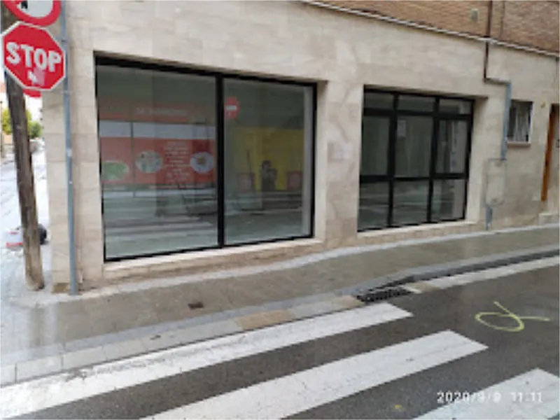 Edificio con fachada de tienda con dos grandes ventanales, paso de peatones y señal de pare en una calle de la ciudad.