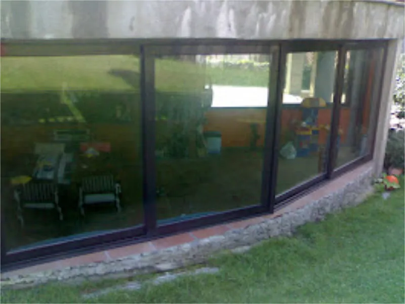 Un edificio curvo con grandes ventanas de color oscuro que reflejan una escena al aire libre, que incluye sillas y follaje.