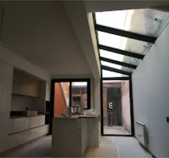 Vista interior de una cocina moderna y un pasillo en construcción, con un tragaluz y una puerta de vidrio que se abre a un patio.