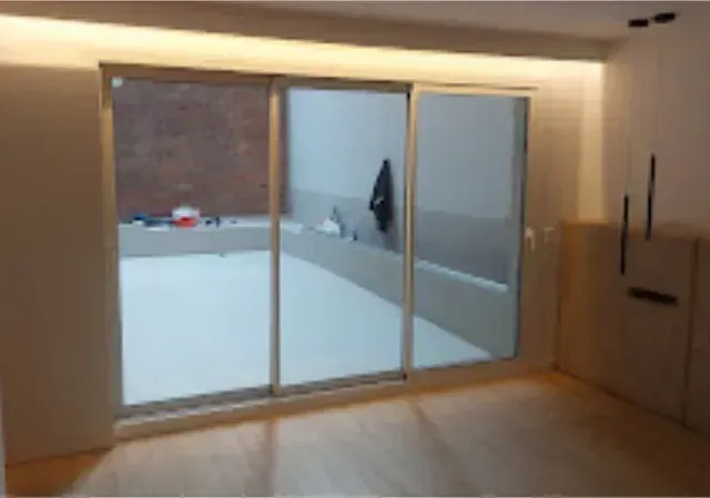 Vista interior con una gran puerta corrediza de vidrio que da a un patio. La habitación tiene pisos de madera y armarios empotrados.