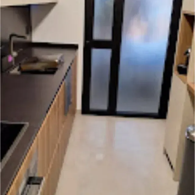 Cocina moderna con encimeras oscuras, gabinetes de madera clara y una puerta de vidrio esmerilado.