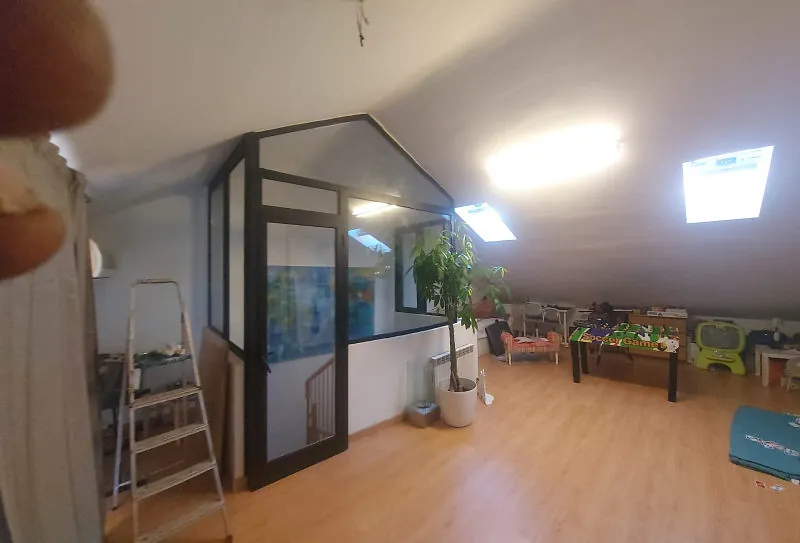 Interior de loft con estructura acristalada, escalera y muebles dispersos. La habitación cuenta con claraboya y suelo de madera.