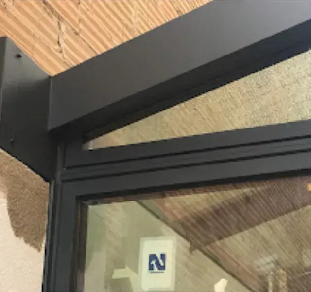 Un primer plano de un toldo de metal negro sobre una ventana contra una pared de ladrillos texturizados.