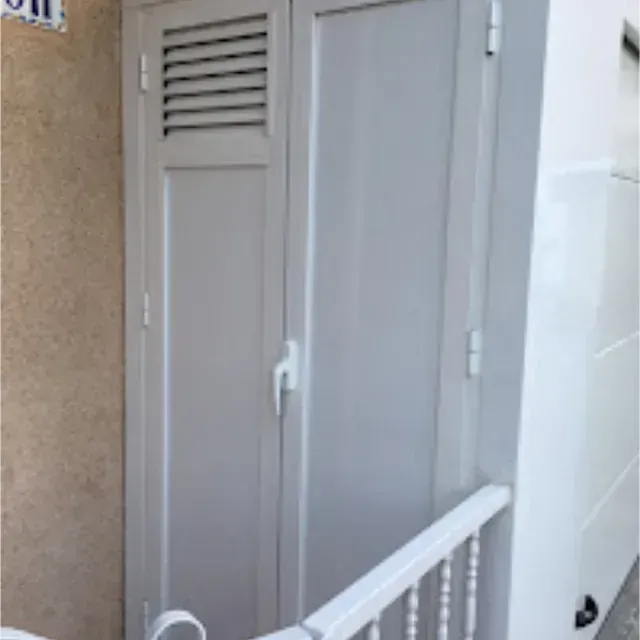 Armario blanco con ventilación en la puerta izquierda, junto a una barandilla y una pared blancas. La pared de atrás es color canela.