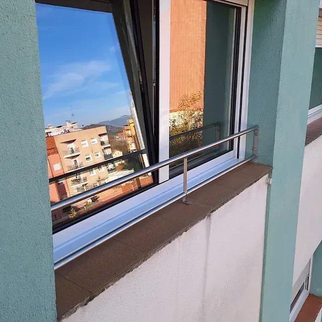 Una ventana con una vista reflejada del paisaje urbano. La ventana está ligeramente abierta y tiene una barra de acero inoxidable.