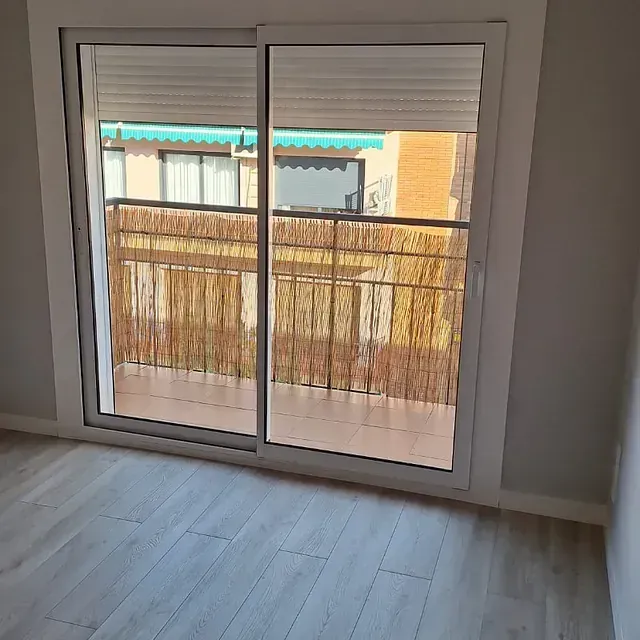 Puerta corrediza de vidrio con balcón. El balcón tiene una mampara de bambú y vistas a la ciudad.