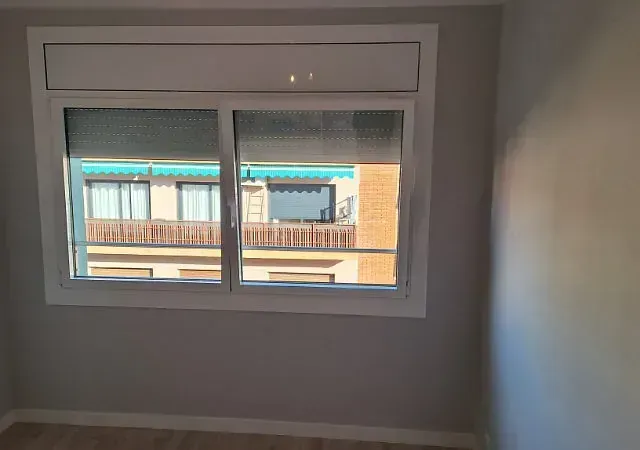 Una ventana con marco blanco en una habitación con paredes grises. Se ven edificios a través de ella.