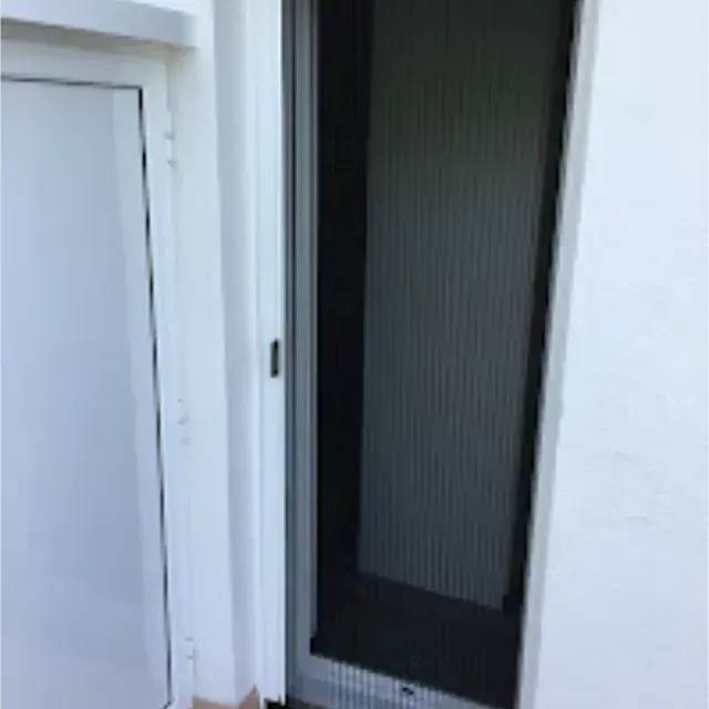 Una puerta blanca y una mosquitera están abiertas, montadas en un marco blanco sobre una pared blanca. La mosquitera es negra.