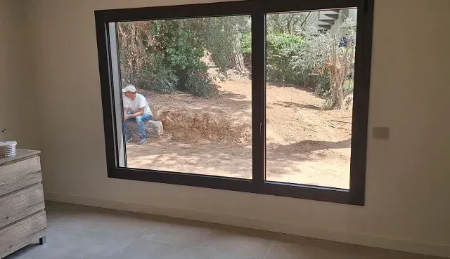 Una persona está sentada frente a una ventana mirando hacia una habitación. La ventana tiene un marco oscuro; el interior es de tonos neutros.