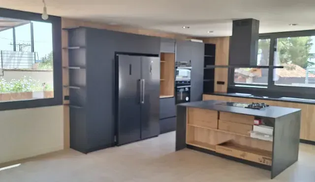Cocina moderna con gabinetes de color gris oscuro y una isla y detalles de pared de madera clara.