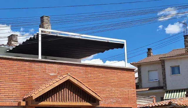 Un edificio de ladrillo con un toldo retráctil con marco blanco en el techo, contra un cielo azul.