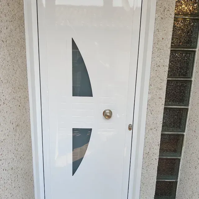 Puerta blanca con un panel de vidrio curvado y un pomo plateado, junto a una columna de ladrillos de vidrio.