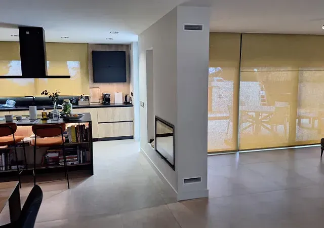 Cocina y sala de estar modernas con paredes de color amarillo pálido, gabinetes de madera y grandes ventanas con cortinas amarillas.