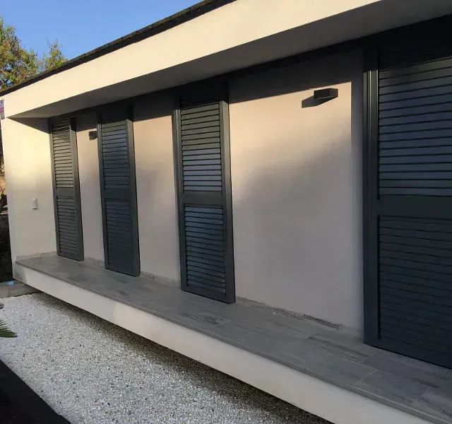 Exterior de un edificio moderno con persianas grises, una pared blanca y un camino de grava.