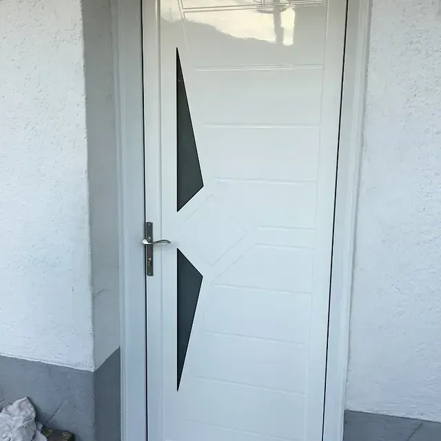 Puerta blanca con detalles geométricos de vidrio negro y manija plateada en una entrada blanca.