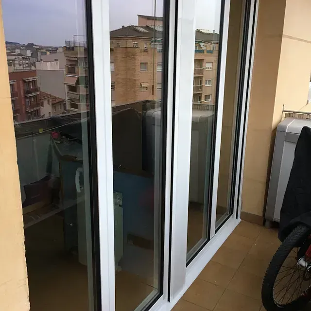 Puertas corredizas de vidrio con marcos blancos, con vista a la ciudad. A la derecha, una rueda de bicicleta.