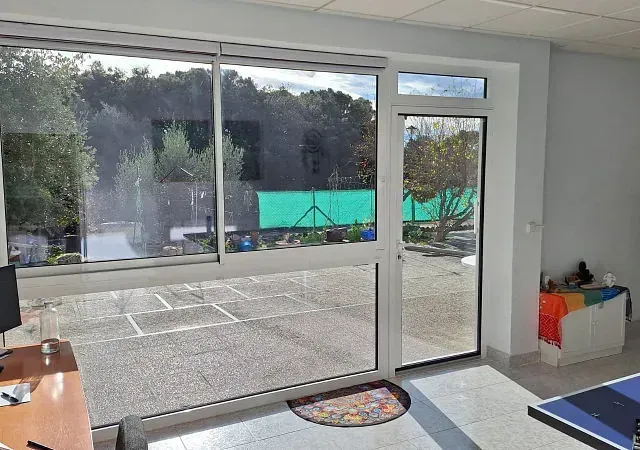 Vista interior con un gran ventanal y una puerta de cristal que da a un patio. El ventanal está junto a una puerta que da al exterior.