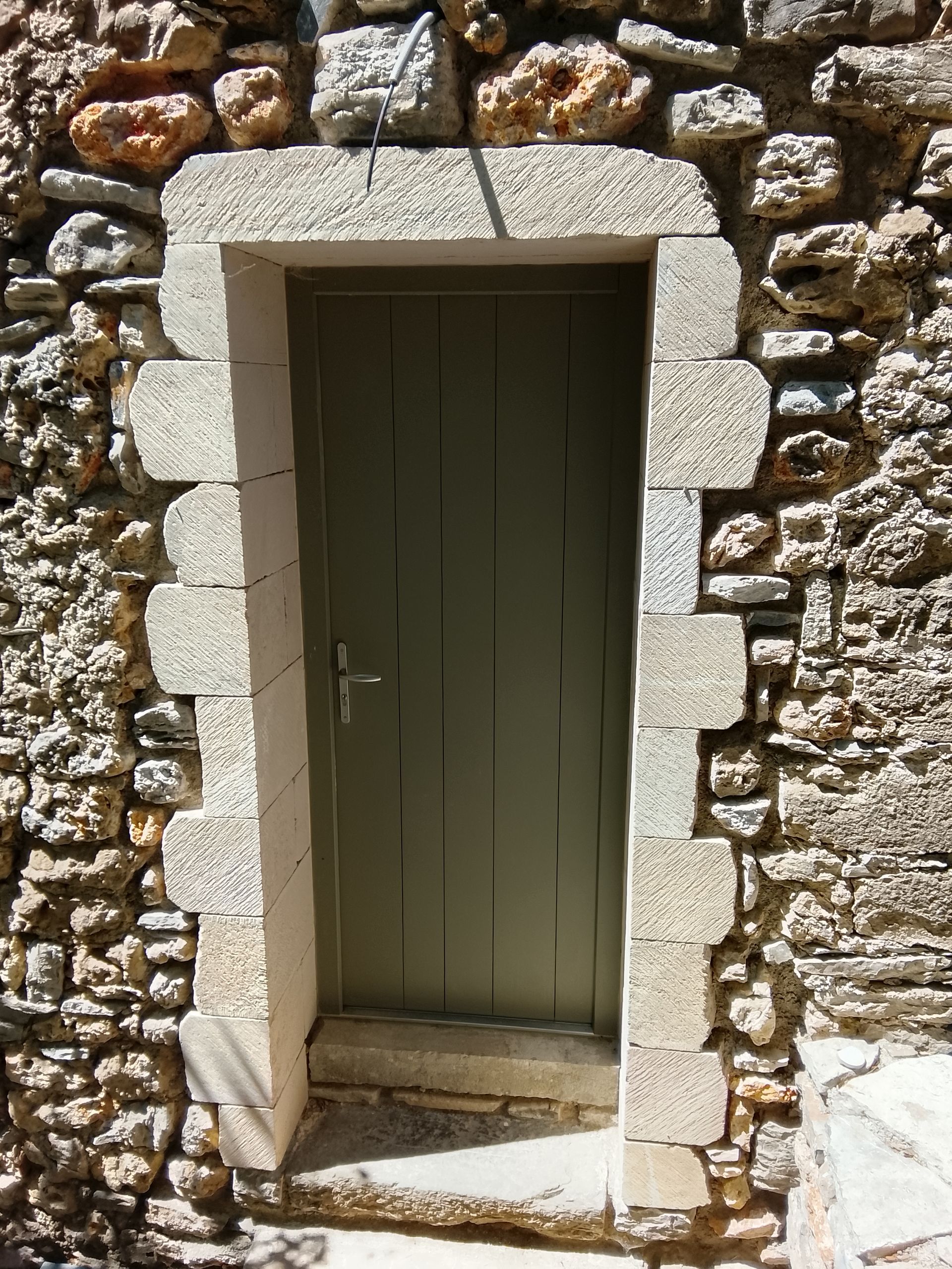 Porte verte dans un mur de pierre, encadrée de blocs de pierre claire.