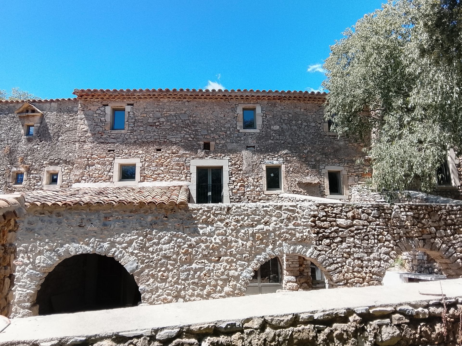 Bâtiment en pierre avec des ouvertures cintrées et des fenêtres se détachant sur un ciel bleu.