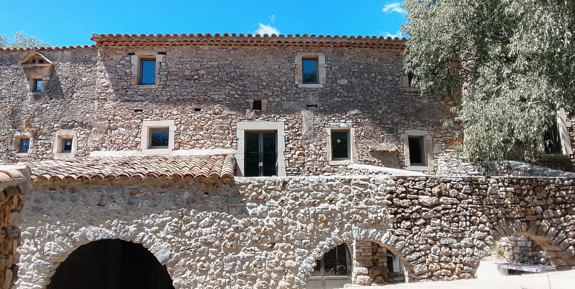 Bâtiment en pierre avec entrée cintrée et nombreuses fenêtres, ciel bleu en arrière-plan.