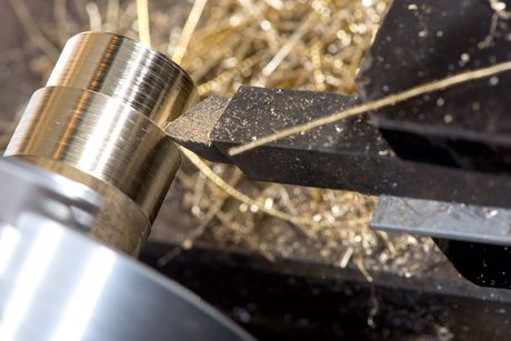 Une pièce cylindrique en laiton usinée sur un tour, générant des copeaux de laiton.