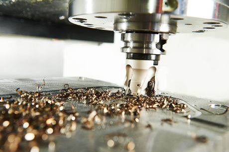 Machine CNC découpant du métal, produisant des copeaux couleur bronze. Gros plan dans un atelier.